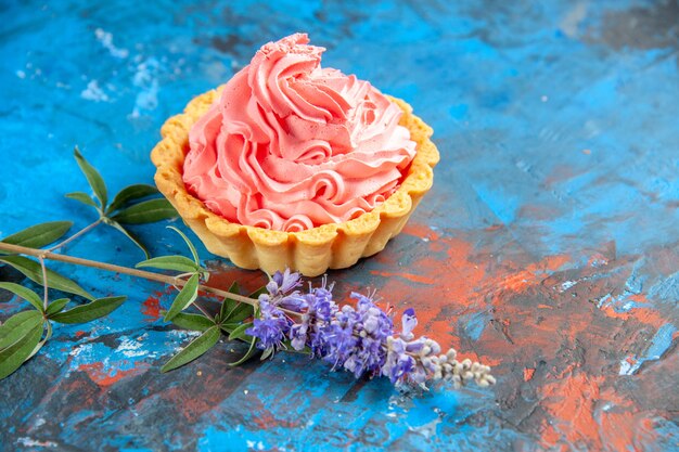 Vista inferior tarta pequeña con crema pastelera rosa flores púrpuras en lugar libre de mesa azul