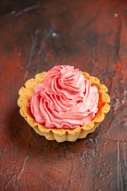 Vista inferior tarta pequeña con crema pastelera rosa sobre mesa rojo oscuro