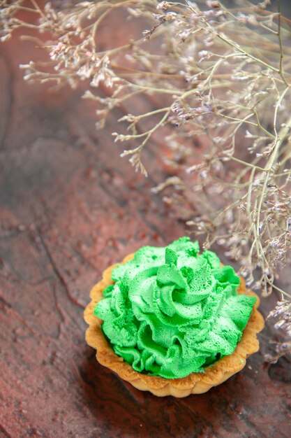 Vista inferior tarta pequeña con crema pastelera verde sobre mesa rojo oscuro