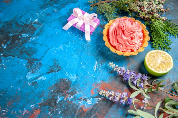 Vista inferior tarta pequeña con rodaja de limón crema pastelera rosa en el espacio libre de la mesa azul