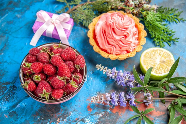 Vista inferior tarta pequeña con tazón de rodaja de limón crema pastelera rosa con frambuesas en el cuadro azul