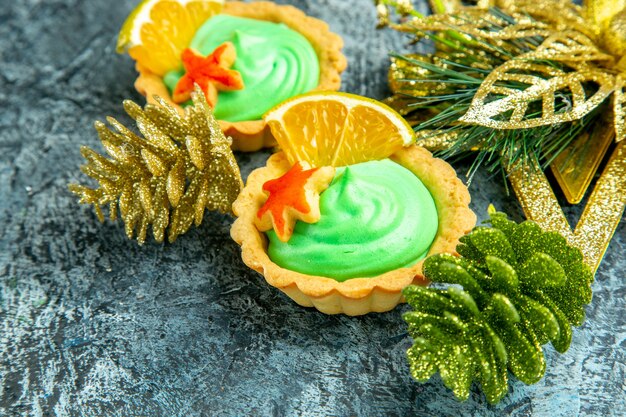 Vista inferior tartas pequeñas con adornos navideños de crema pastelera verde sobre superficie gris