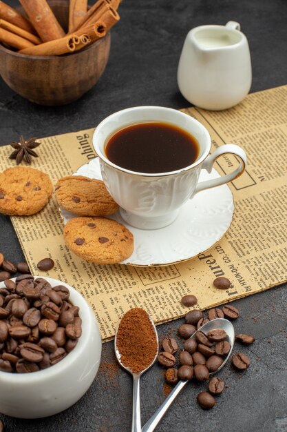 Vista inferior de la taza de café tostado granos de café y canela en tazones de galletas en la oscuridad