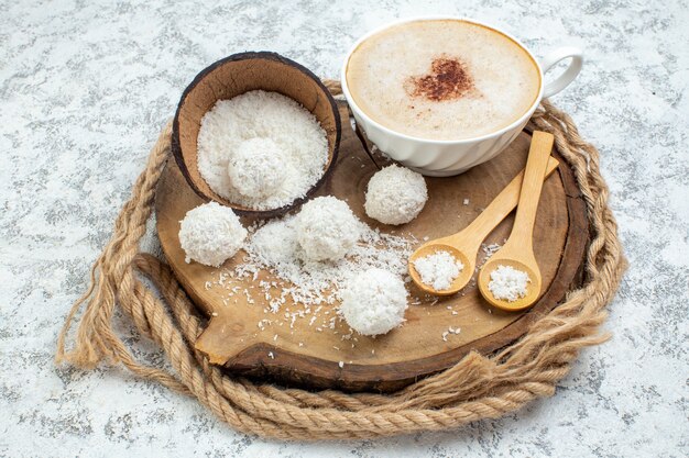 Vista inferior de la taza de capuchino con cucharas de madera en polvo de coco sobre tablero de madera sobre fondo gris