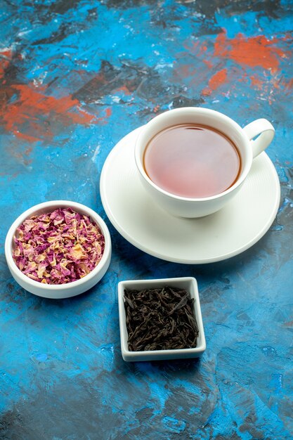 Vista inferior de una taza de cuencos de té con pétalos de flores secas y té en la superficie azul roja