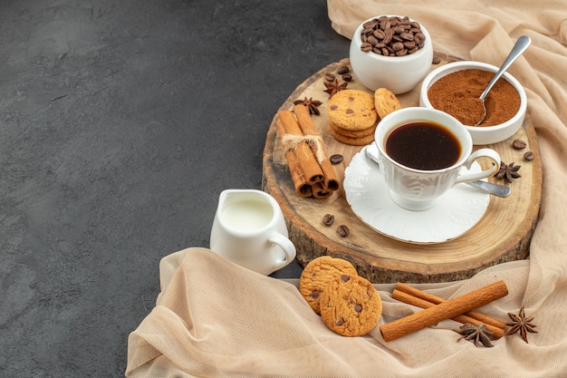 Vista inferior de la taza de galletas de café, palitos de canela, taza de leche, tablero de madera en la oscuridad.