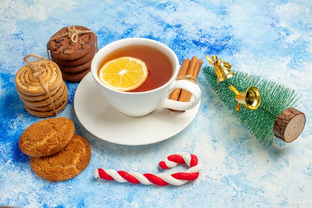 Vista inferior de la taza de galletas de té atadas con una cuerda pequeño árbol de Navidad y dulces en la mesa azul