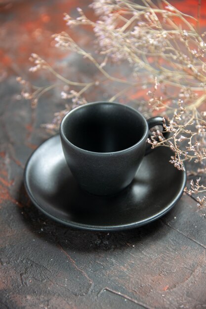 Vista inferior taza negra y plato de flores secas de la rama sobre la mesa de color rojo oscuro
