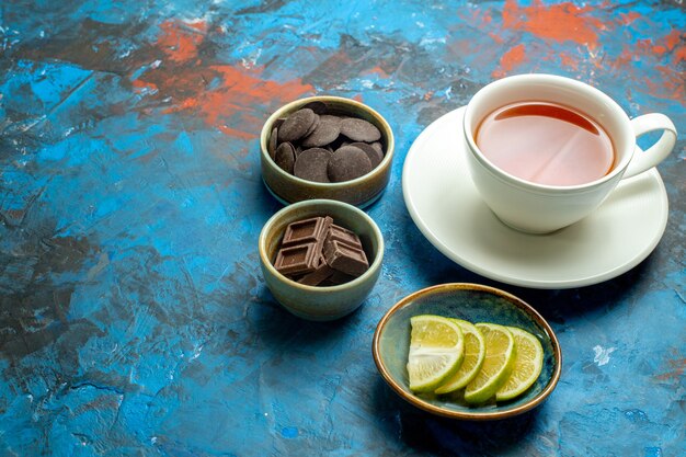Vista inferior de una taza de té, chocolates y rodajas de limón en el espacio libre de la superficie roja azul