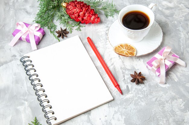 Vista inferior de una taza de té, cuaderno, lápiz, pequeño regalo, árbol de Navidad, juguete sobre fondo gris