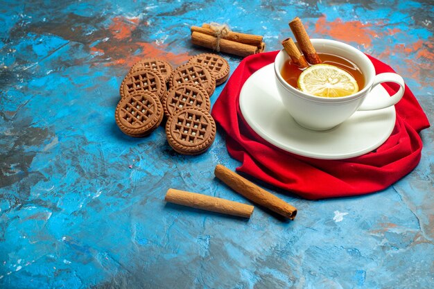 Vista inferior de una taza de té con limón y canela, galletas de mantón rojo en el lugar de la copia de la superficie roja azul