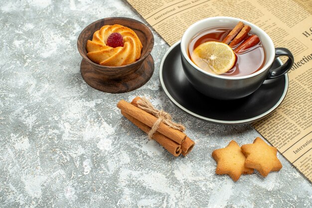 Vista inferior de una taza de té con rodajas de limón y canela en galletas de periódico sobre superficie gris