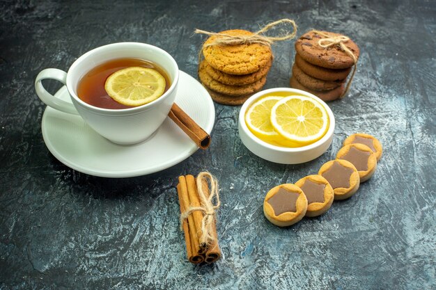 Vista inferior de una taza de té con sabor a limón y galletas de canela con galletas de chocolate atadas con una cuerda, palitos de canela, rodajas de limón en un tazón sobre la mesa gris