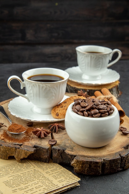 Vista inferior tazas de té, galletas, canela, anís, granos de café en un tazón en la oscuridad.