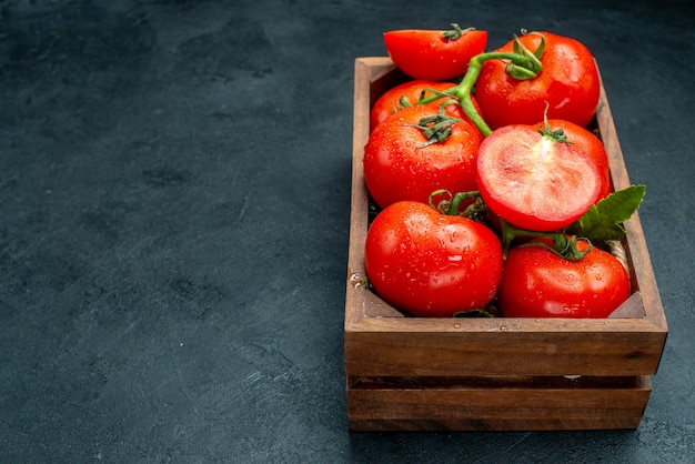 Vista inferior de tomates rojos en caja de madera sobre mesa negra con espacio libre