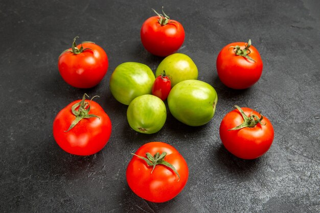Vista inferior de tomates rojos y verdes alrededor de un tomate cherry sobre fondo oscuro