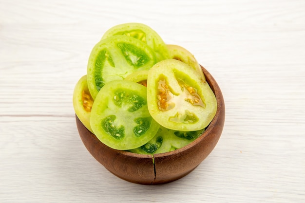 Vista inferior de tomates verdes picados en un tazón en el cuadro blanco