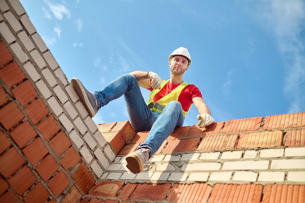 Foto gratuita vista inferior del trabajador sentado en la pared de ladrillo