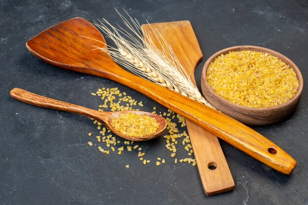 Vista inferior de trigo bulgur en un tazón y una cuchara de madera dos grandes cucharas de madera en la mesa