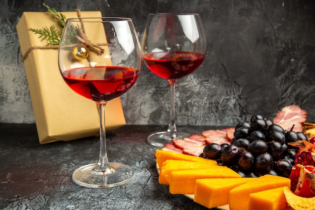 Vista inferior de trozos de queso carne uvas y granada en tablero ovalado vaso de vino regalo de navidad en la oscuridad