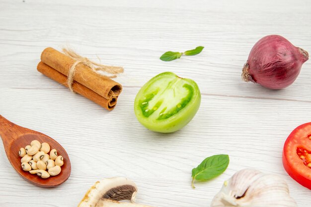 Vista inferior verduras frescas cuchara de madera setas tomates verdes y rojos cebolla canela en rama ajo en mesa gris