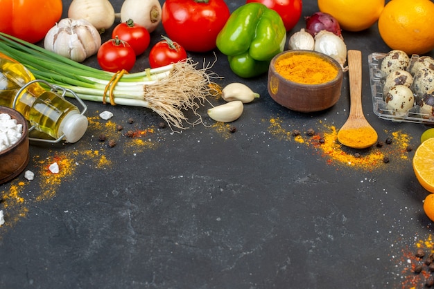 Vista inferior de verduras frescas cúrcuma en un tazón pequeño y una cuchara de madera botella de aceite huevos de codorniz en el espacio libre de la mesa