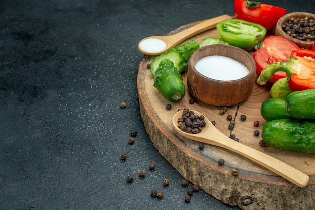 Vista inferior de verduras frescas pepinos pimienta negra y sal en cucharas de madera y tazones de fuente tomates rojos y verdes pimiento sobre tablero de madera en el espacio libre de la mesa oscura