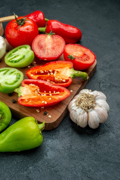 Vista inferior de verduras frescas setas tomates rojos y verdes pimientos en la tabla de cortar ajo pimienta negra en un tazón sobre la mesa oscura