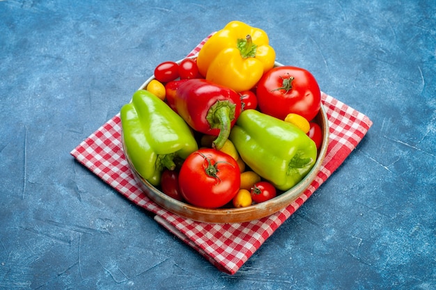 Foto gratuita vista inferior verduras frescas tomates cherry diferentes colores pimientos tomates cumcuat en un plato sobre una toalla de cocina a cuadros roja blanca sobre una superficie azul