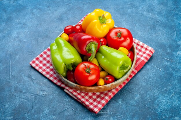 Vista inferior verduras frescas tomates cherry diferentes colores pimientos tomates cumcuat en un plato sobre una toalla de cocina a cuadros roja blanca sobre una superficie azul