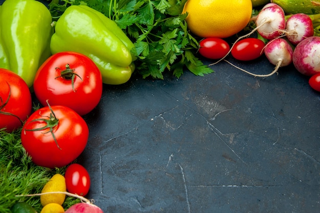 Vista inferior de verduras frescas tomates rábano perejil eneldo tomates cherry pimientos limón sobre una superficie oscura con lugar de copia