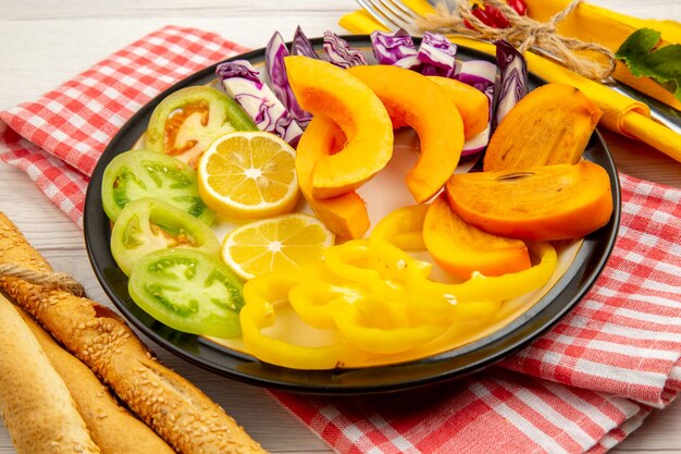 Vista inferior verduras y frutas picadas caquis calabaza limones tomates verdes pimientos en un plato negro pimiento rojo en polvo sal marina pimienta negra en tazones pequeños pan en la mesa