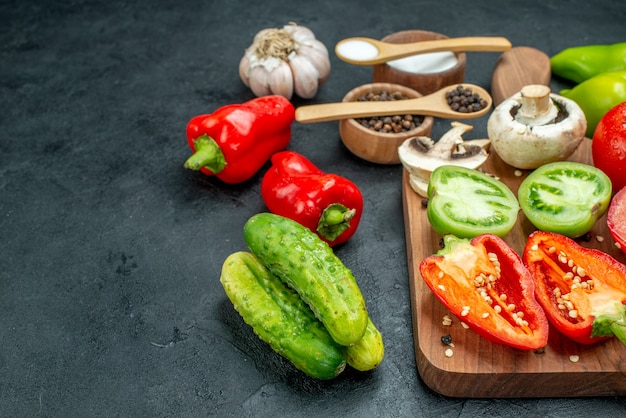 Vista inferior verduras setas tomates rojos y verdes pimientos rojos en tabla de cortar ajo pimienta negra y sal en tazones cucharas de madera pepinos en el espacio de copia de mesa oscura