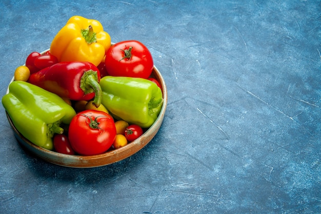 Vista inferior de verduras tomates cherry pimientos tomates de diferentes colores en un plato de madera en la mesa azul con lugar de copia