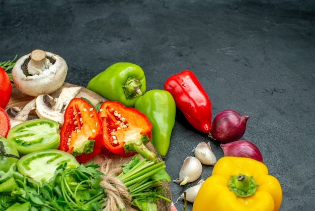 Vista inferior de verduras tomates pimientos rojos verdes setas en tablero rústico pimientos picantes cebolla roja ajo en mesa negra espacio libre