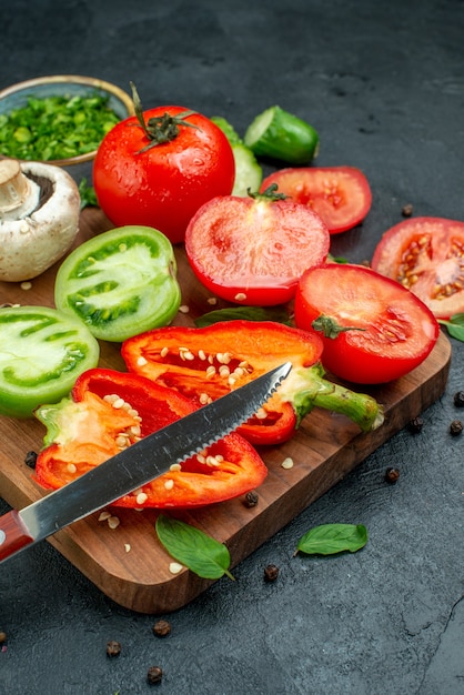 Vista inferior verduras tomates verdes y rojos pimientos cuchillo en la tabla de cortar verduras en un tazón en el cuadro negro