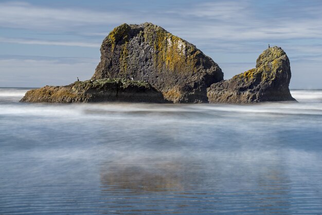 Vista de una isla misteriosa con su reflejo en la superficie del mar sobre un fondo de día nublado