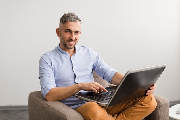 Vista larga hombre usando su computadora portátil y sonrisas