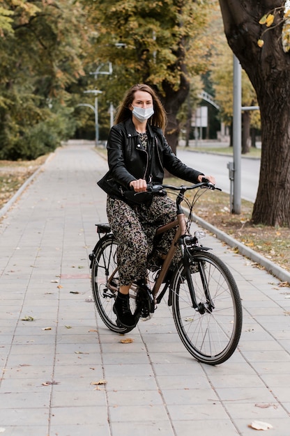 Foto gratuita vista a largo plazo de mujer con máscara y andar en bicicleta