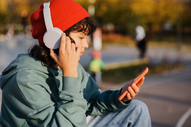 Vista lateral del adolescente escuchando música con auriculares mientras usa el teléfono inteligente