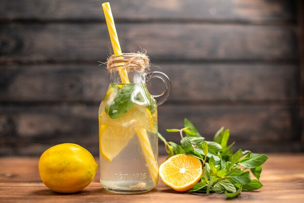 Vista lateral del agua de desintoxicación fresca natural servida con un tubo de menta y naranja sobre un fondo marrón