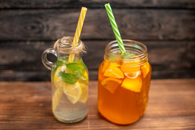 Vista lateral de agua desintoxicante fresca y jugo de frutas servido con tubos sobre un fondo marrón