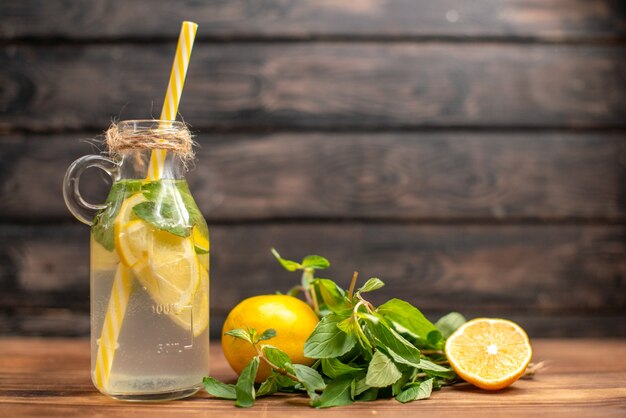 Vista lateral de agua desintoxicante fresca servida con tubo de menta y naranja sobre un fondo marrón