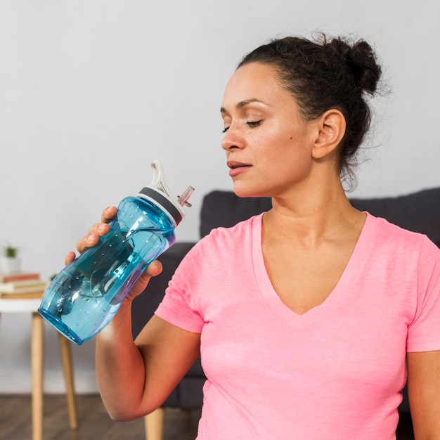 Vista lateral del agua potable de la mujer embarazada mientras hace ejercicio en casa