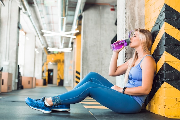 Vista lateral de un agua potable de mujer joven en el gimnasio