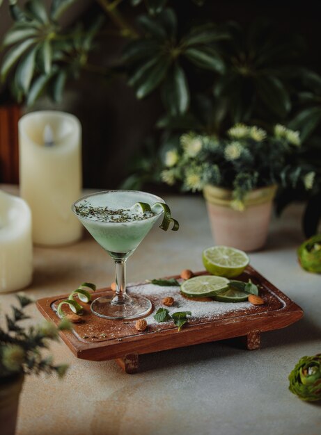 Vista lateral de alcohol coctel con almendras y lima sobre una tabla de madera