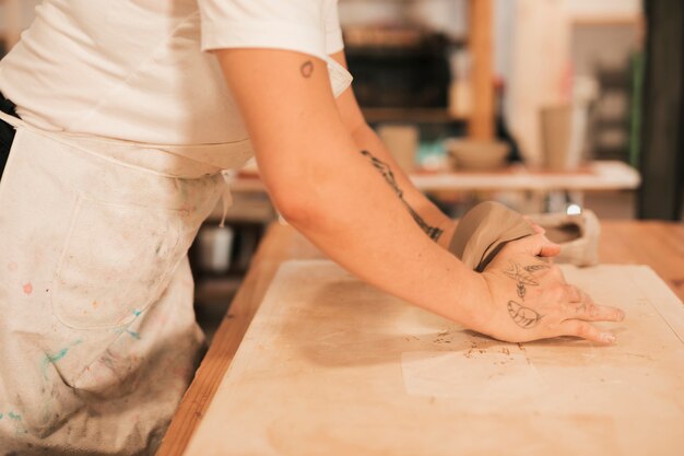 Vista lateral de un alfarero femenino amasando la masa en una mesa de madera