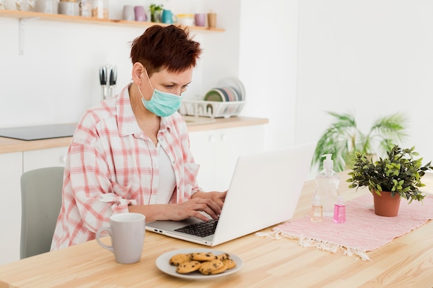 Foto gratuita vista lateral de la anciana con máscara médica trabajando desde casa