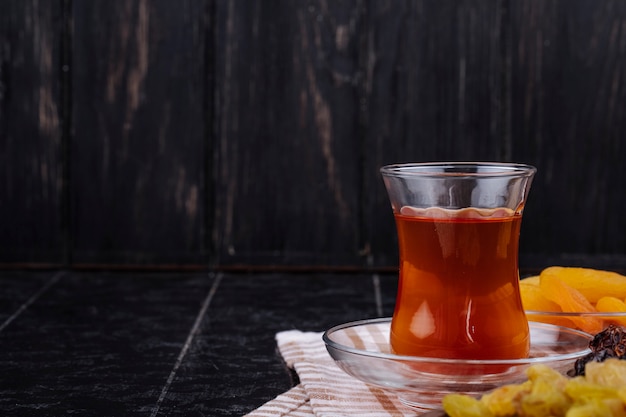 Vista lateral de armudu vaso de té con frutos secos sobre fondo negro rústico