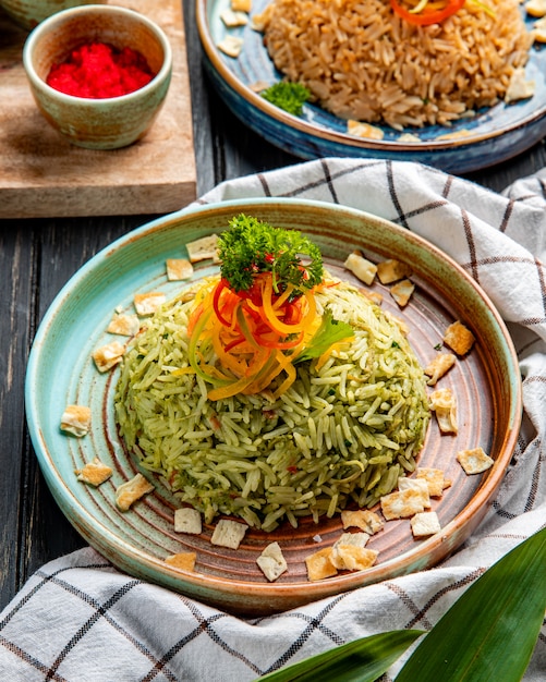 Vista lateral del arroz japonés con verduras en un plato sobre superficie de madera